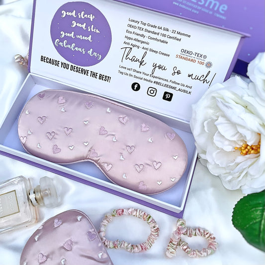 A light pearl pink mulberry silk sleep mask with heart embroidery, presented in an open Belle Esme gift box